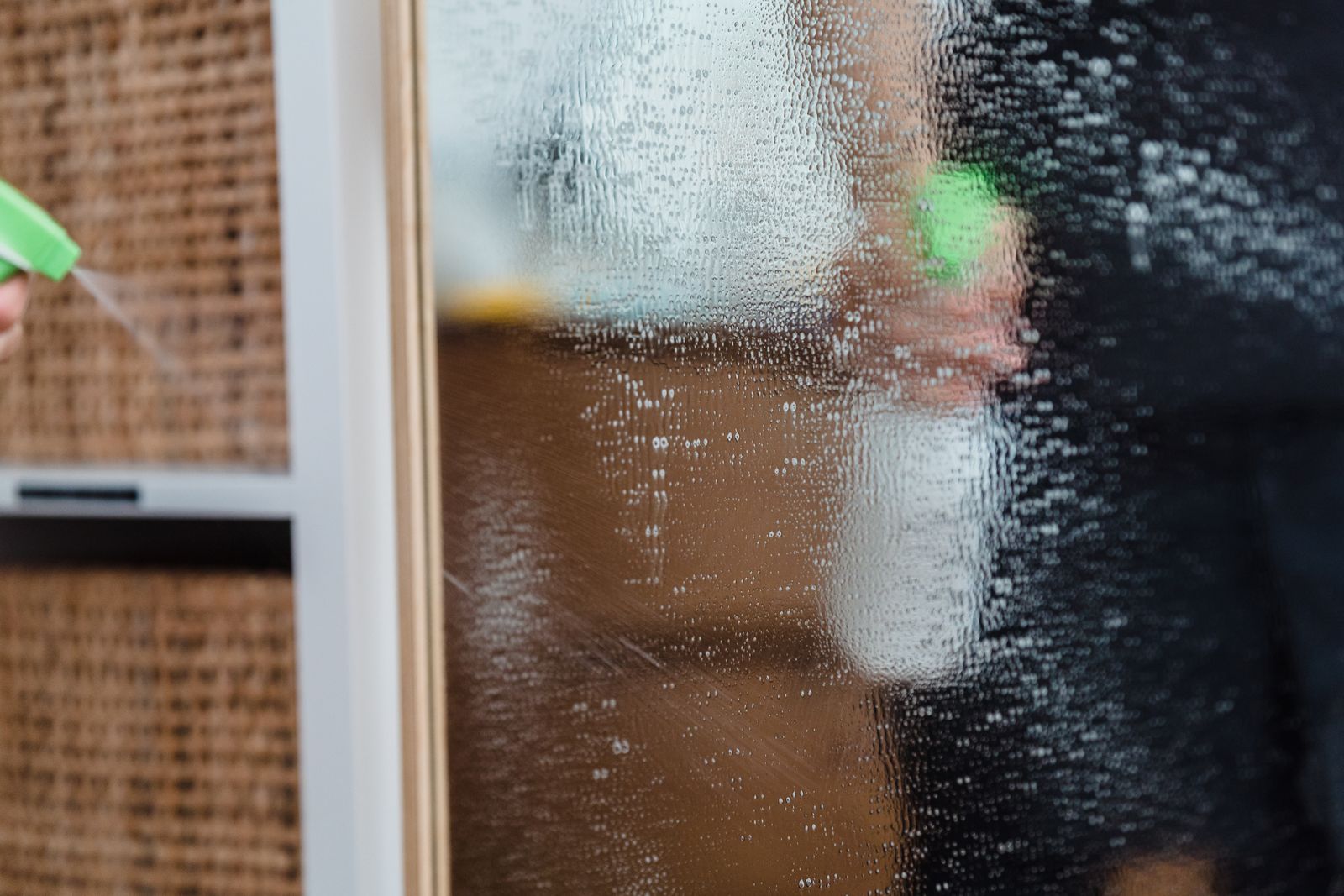 Detailed view of a mirror being cleaned using a water sprayer, indoors.